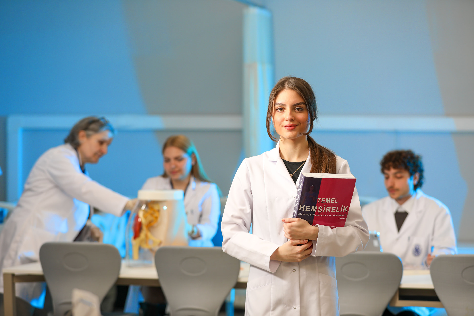 Medical student in a white coat holding a nursing textbook in a teaching laboratory